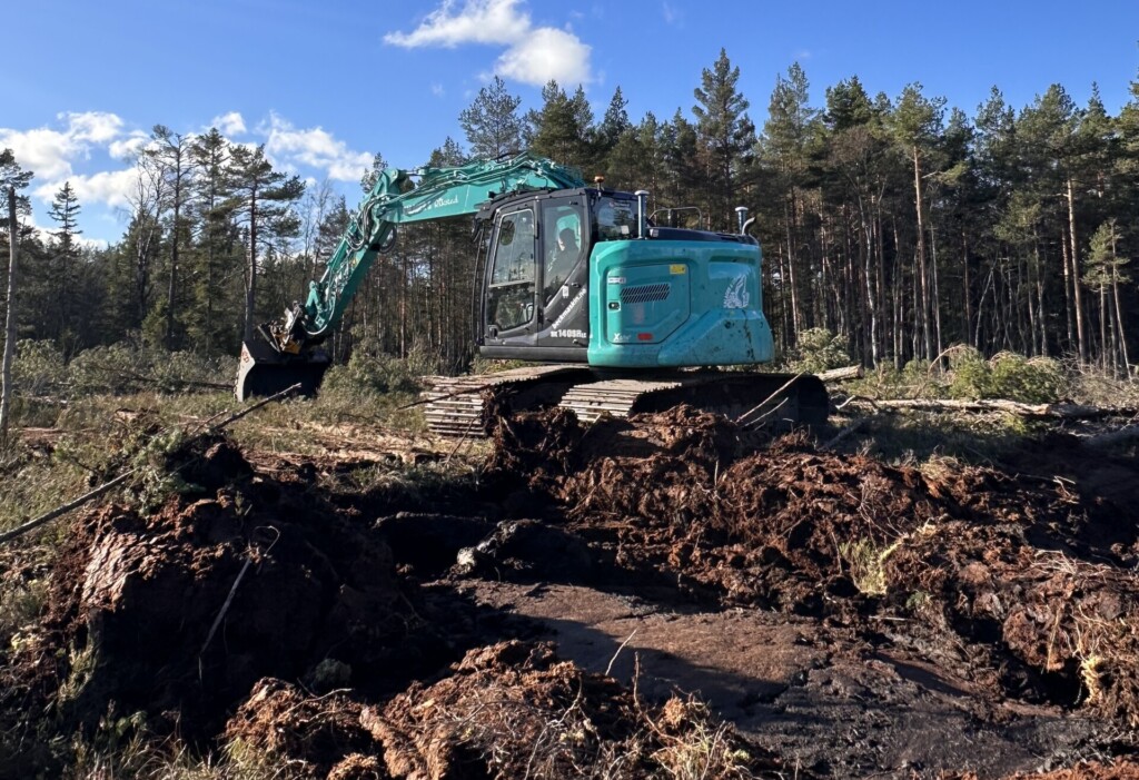 Turkis gravemaskin som graver i en myr