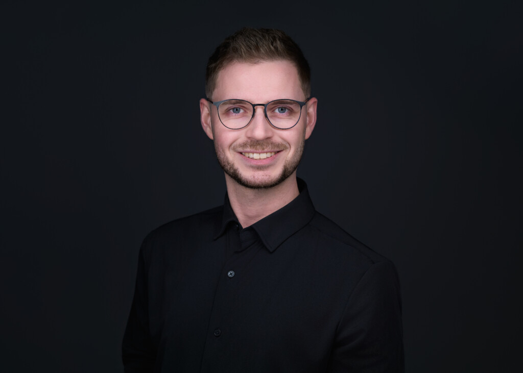 Smilende mann i sort skjorte, briller, bart og skjegg