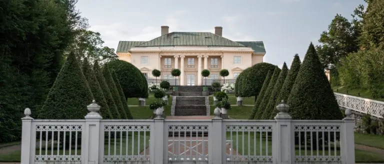 Foto av Gunnebo slott med formklipte spisse trær på rekke