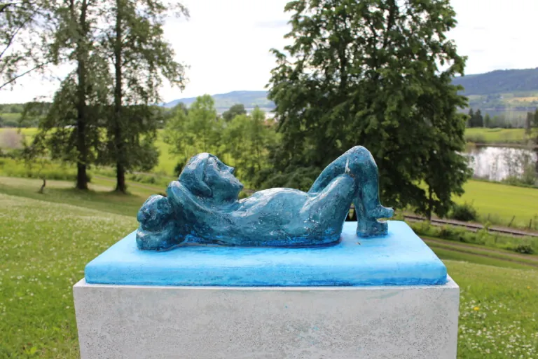 En blåmalt keramisk skulptur av et barn som ligger på ryggen og ser opp på himmelen