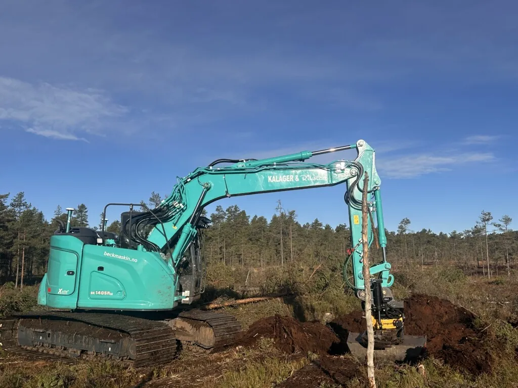 Turkis gravemaskin som graver i myr under knall blå høsthimmel