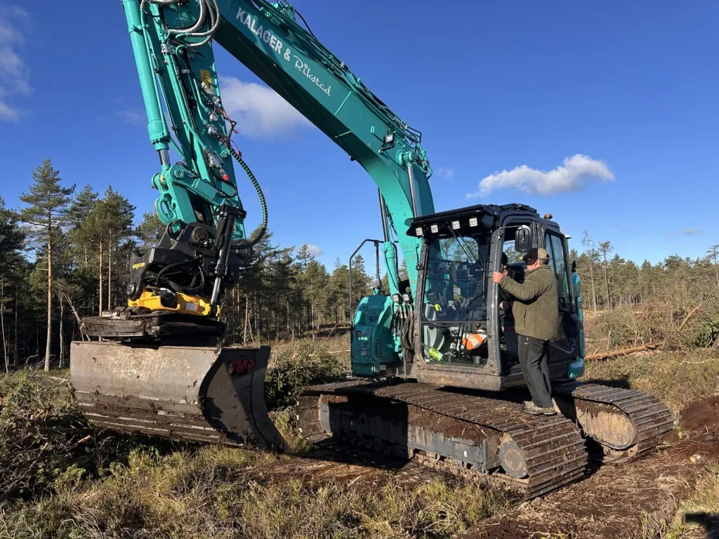 Mann som står på beltet til en gravemaskin