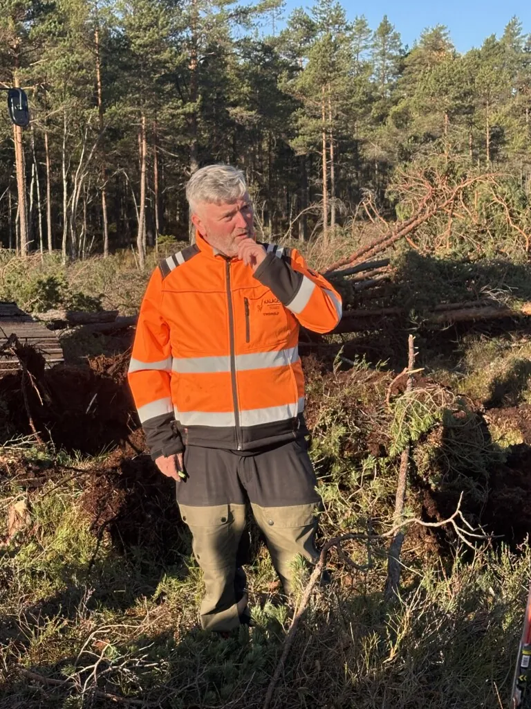 Mann i oransje arbeidsjakke står ute i skogen