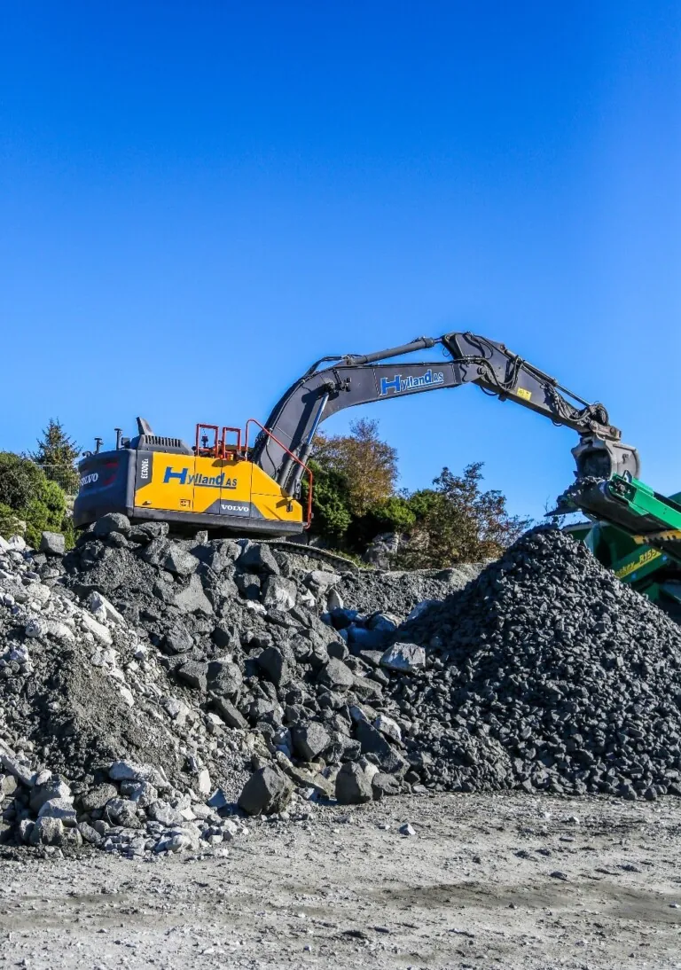 gul gravemaskin som jobber i et anlegg