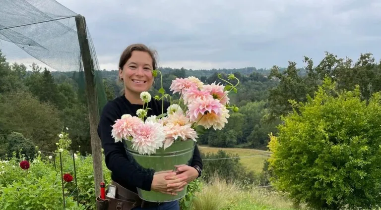 Dame som står ute og holder en bøtte med georginer