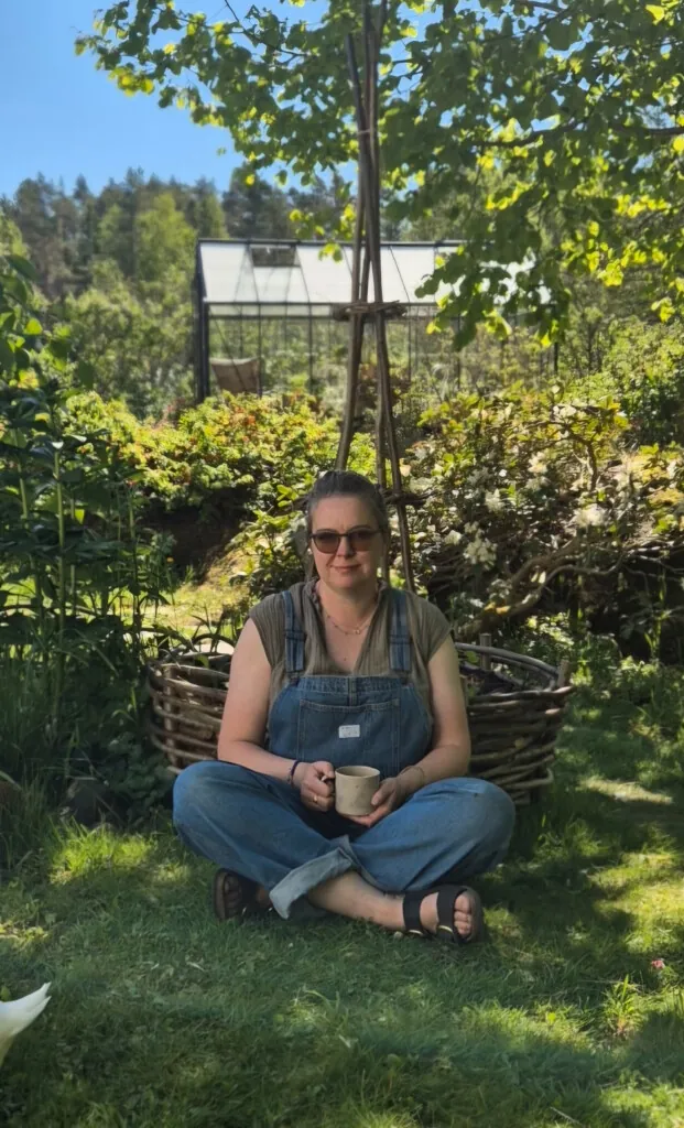 Dame med kaffekopp i hånda sittende i en hage