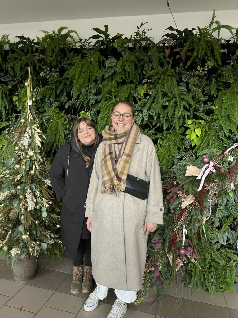 To jenter avbildet foran en grønn plantevegg