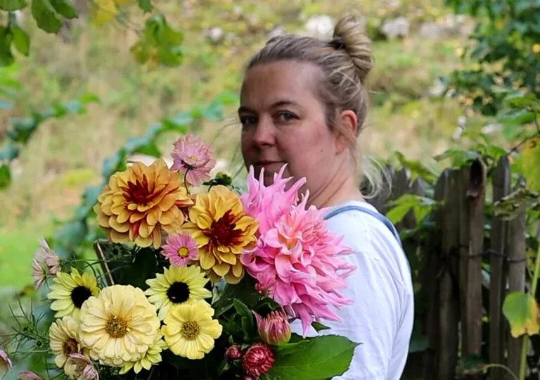 Therese Nybu med en stor blomsterbukett på armen, i hagen på Stabbestad
