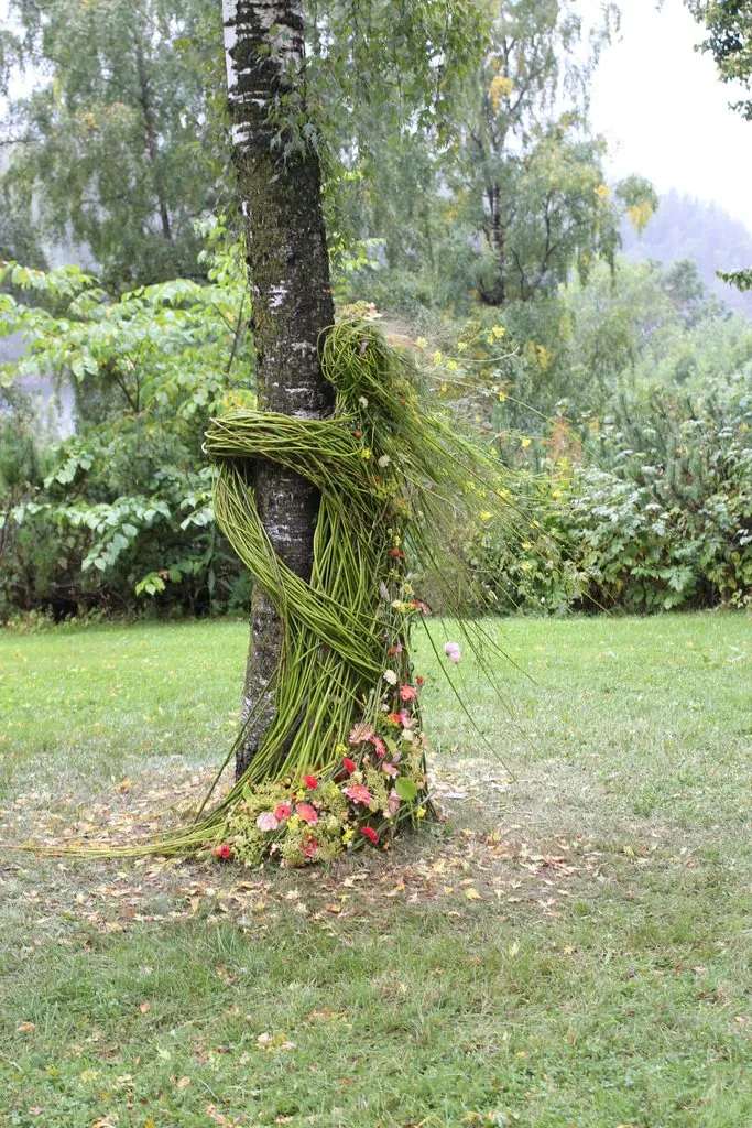 Botanisk arbeid laget av pilgreiner og blomster. Ser ut som ei jente som holder fast i et tre