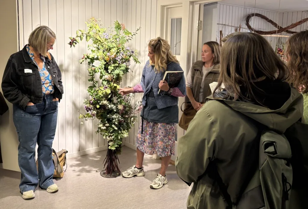 Dame som står ved siden av en blomsterinstallasjon og snakker om den