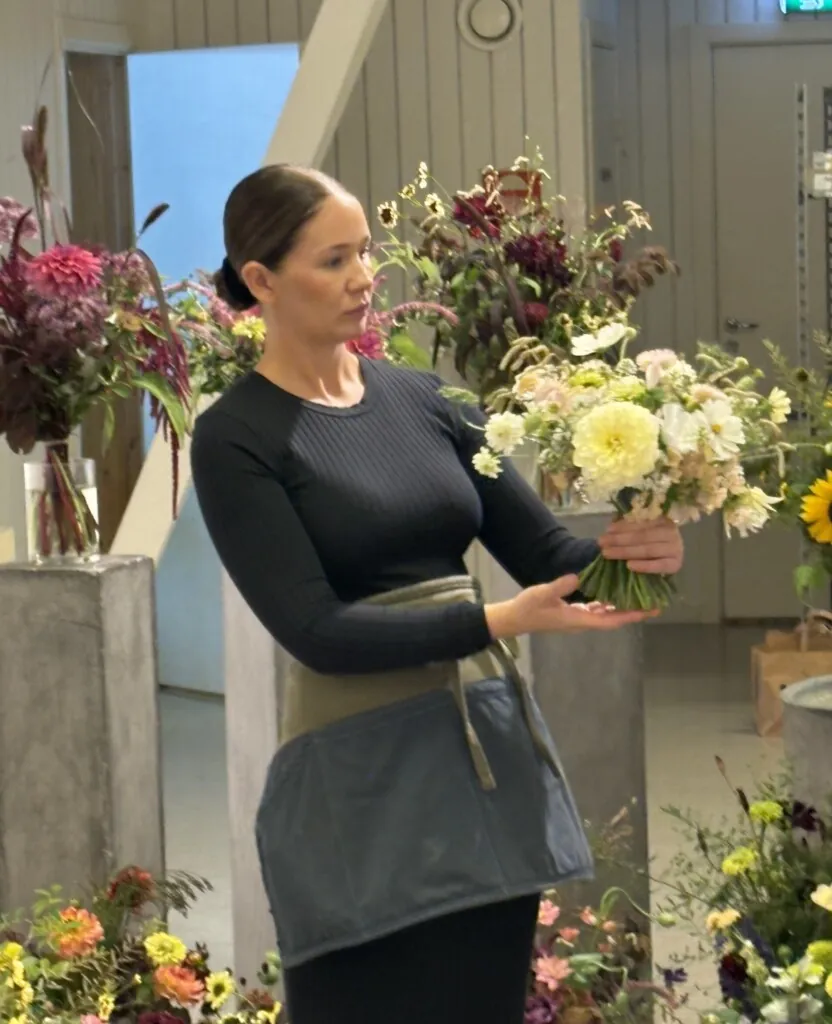 Blomsterdekoratør i svart genser som holder en håndbundet brudebukett.
