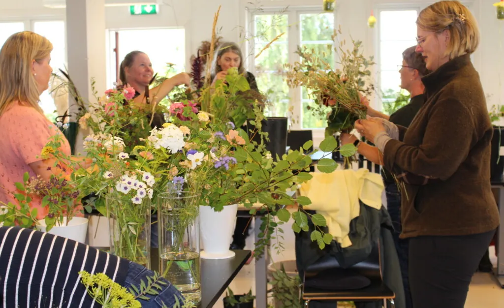 Blomsterdekoratører som står inne i et klasserom og lager buketter