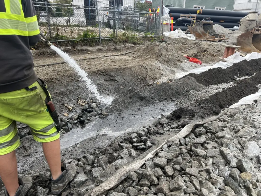 Person i arbeidsklær spyler vann på grus og stein i et uteanlegg
