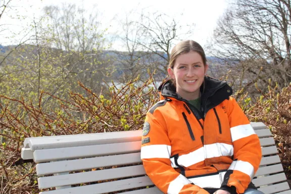 Jente med orange arbeidsjakke som sitter på en benk på Norges grønne fagskole - Vea